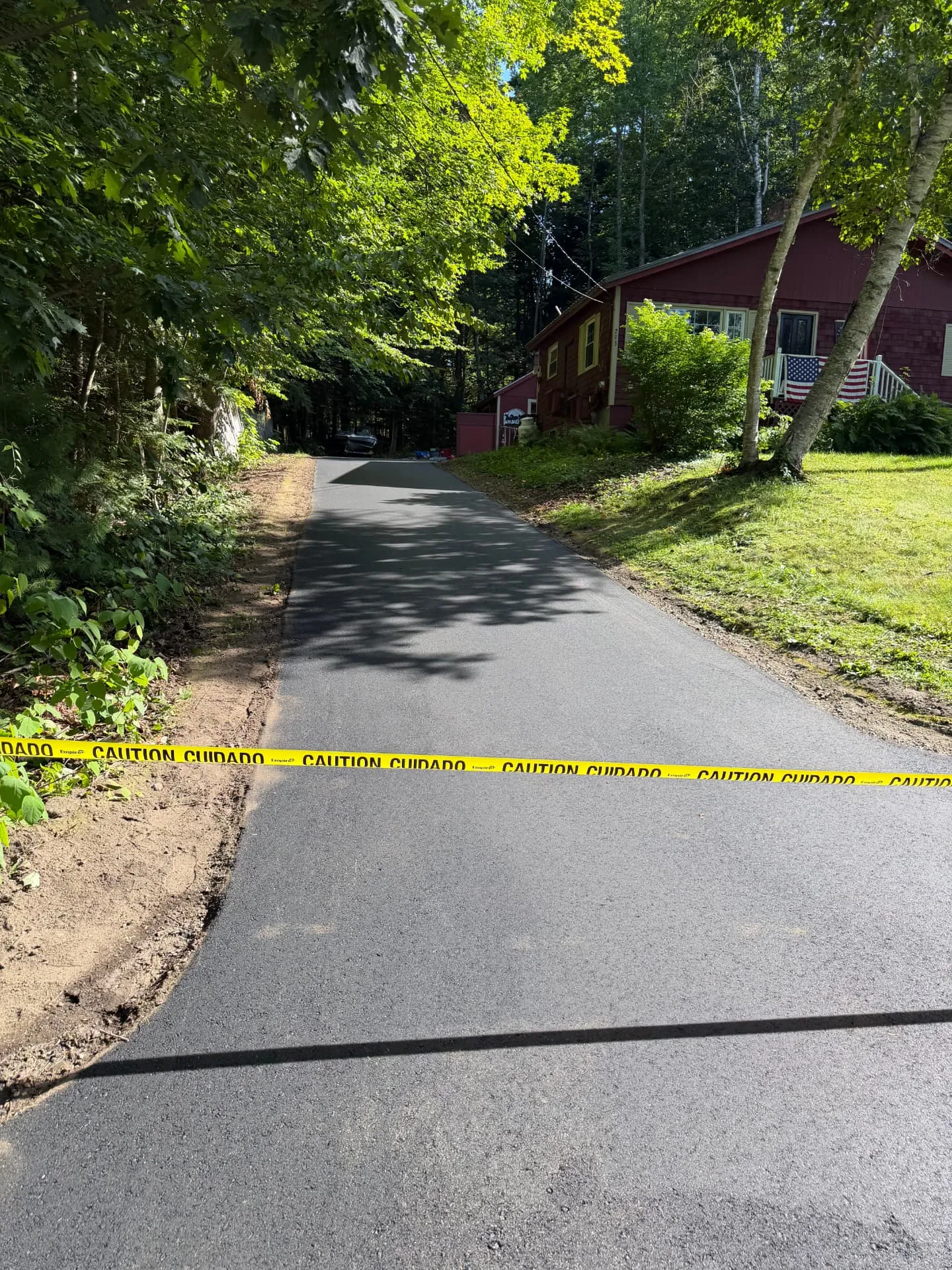 Freshly paved driveway taped off beside a red Maine home