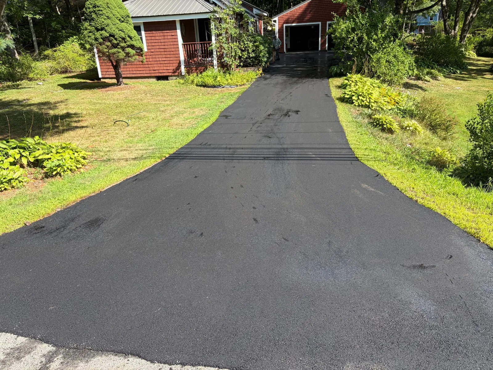 Freshly paved long asphalt driveway leading to a detached garage beside a red cottage in Saco, Maine