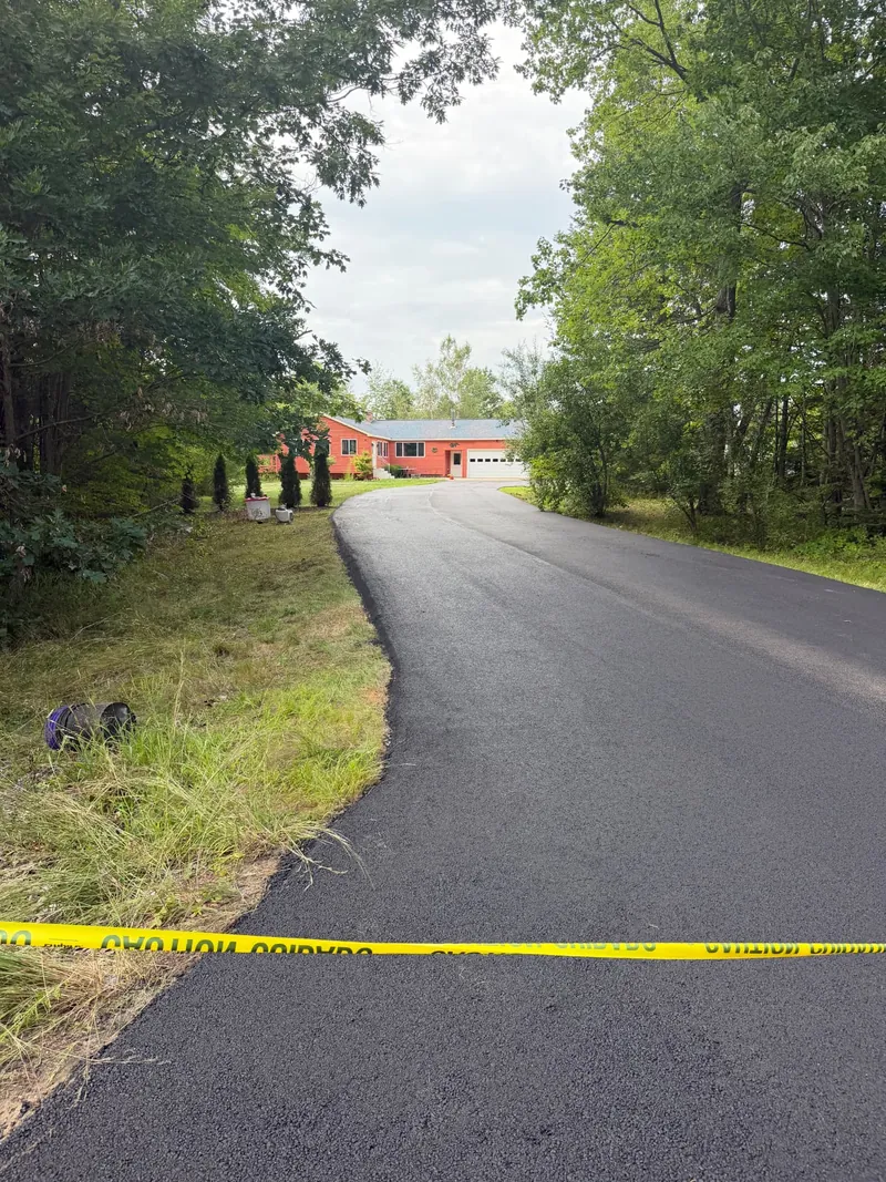 Freshly paved driveway leading to a red ranch home