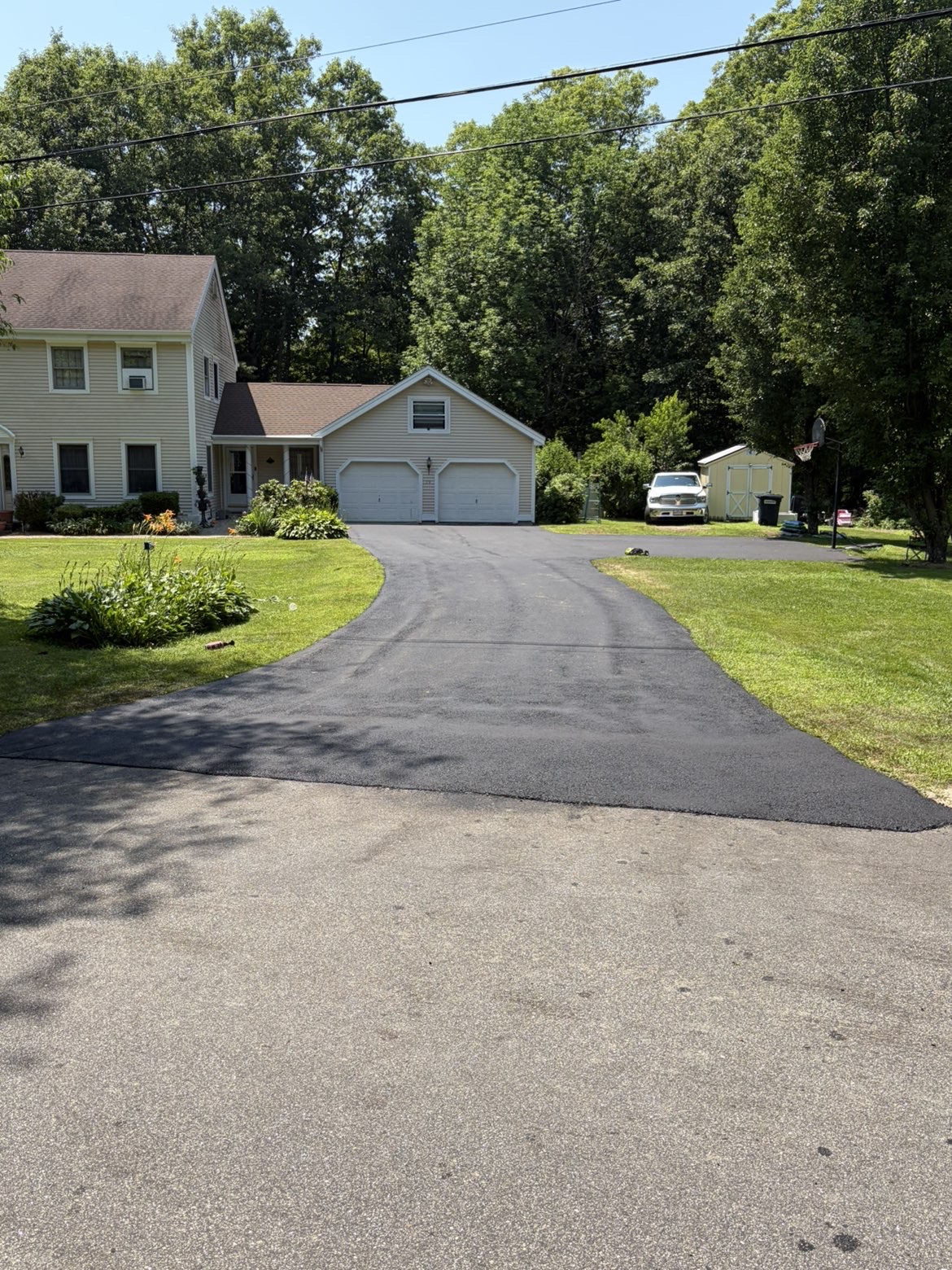 Freshly paved residential asphalt driveway with clean edges and lush green lawn