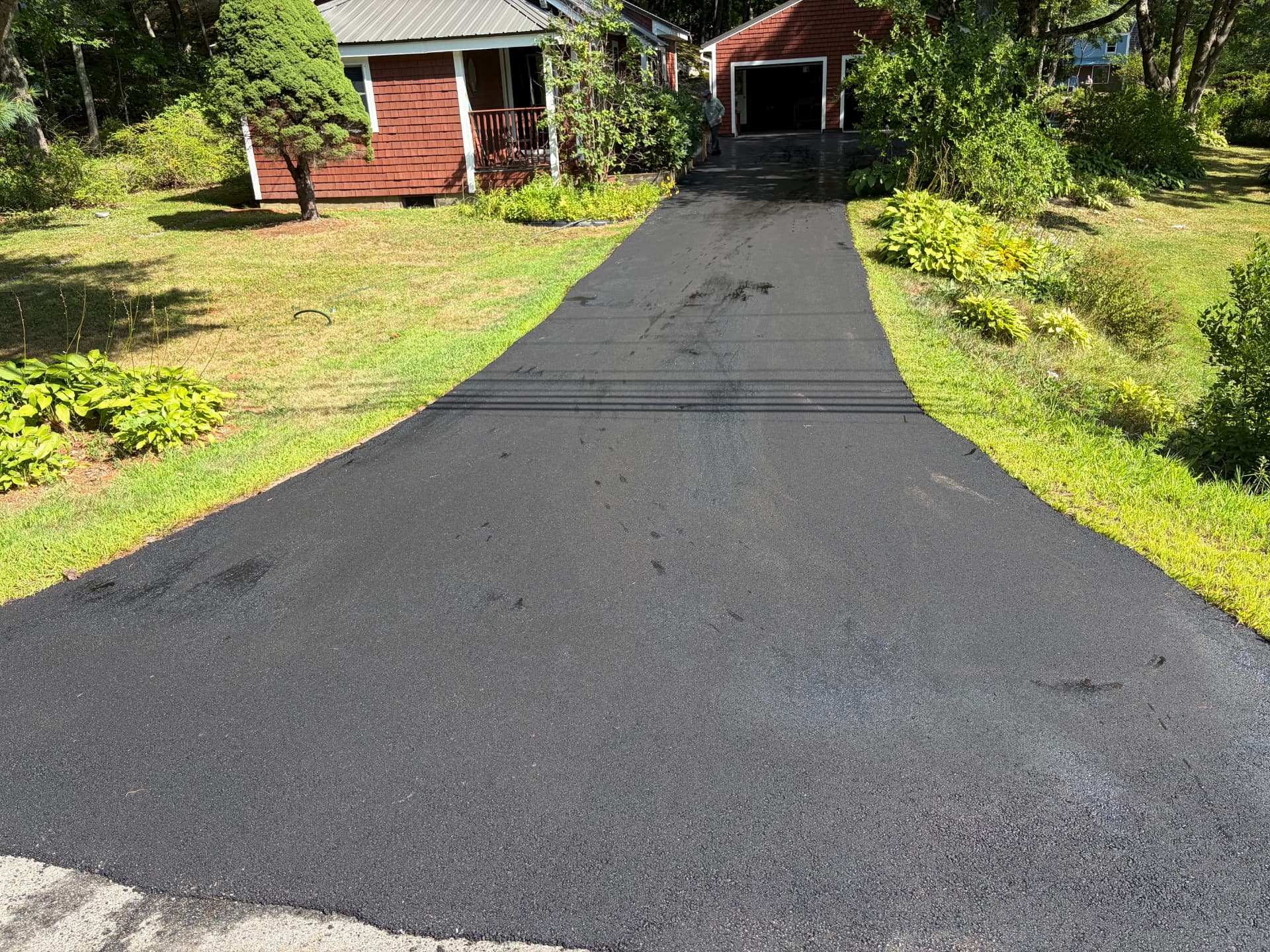 Long freshly paved asphalt driveway running up to a red shingled Maine home and detached garage