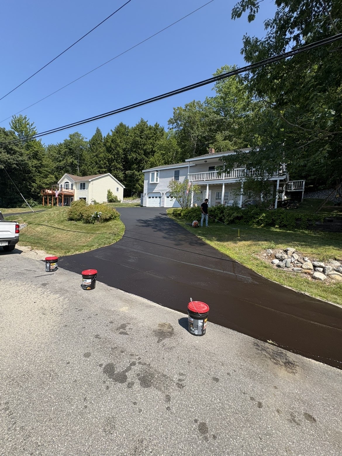 Sealcoating in progress on a sloped residential driveway with buckets of sealer at the road