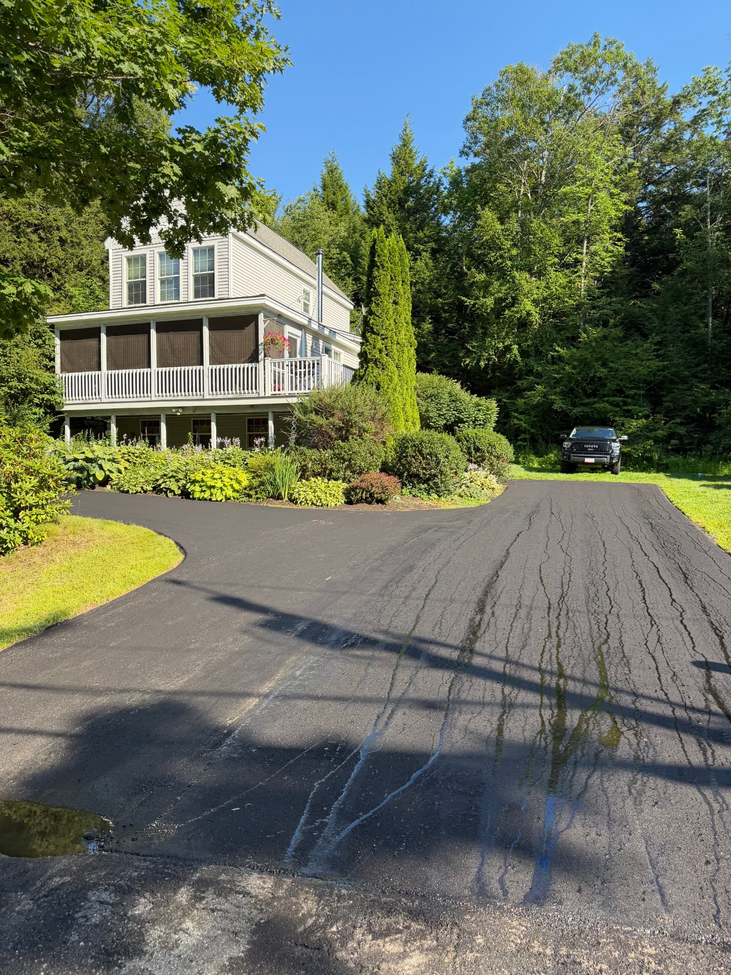 Freshly paved curved asphalt driveway leading up to a Maine home with gardens and a pickup truck