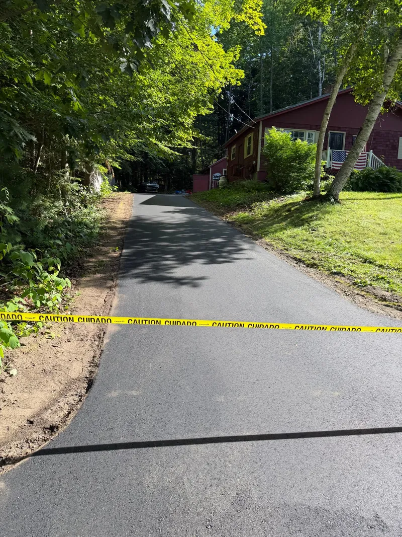 Freshly paved driveway taped off beside a red Maine home