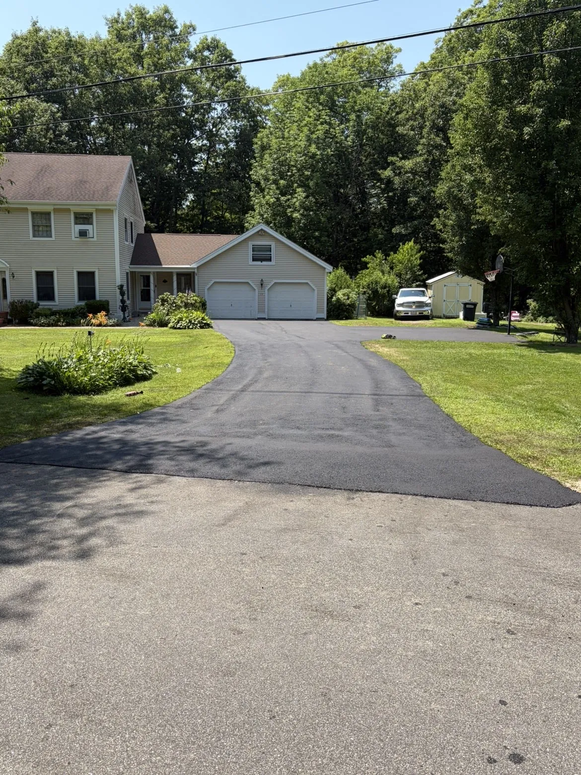 Freshly paved residential asphalt driveway with clean edges and lush green lawn