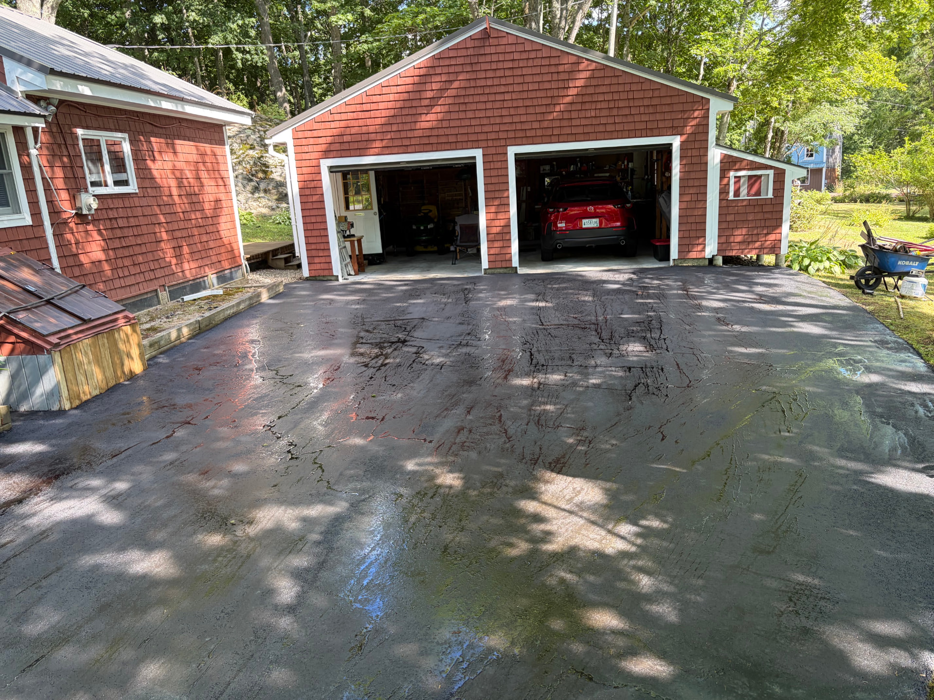 Wide sealcoated parking area in front of a two-bay red garage